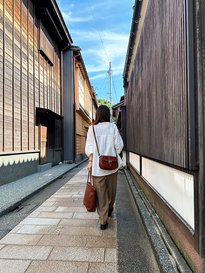 ひがし茶屋街の路地を歩く50代女性と旅行バッグ