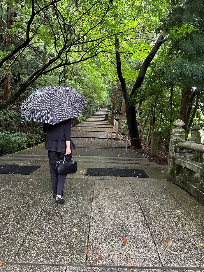 雨の白山比咩神社を訪れる50代女性とシモーヌ・ゼンの黒い本革バッグ